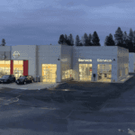 Exterior view of the Wendle Nissan dealership and service center in Spokane, WA, featuring a large inventory of new and used cars and SUVs under evening lights.