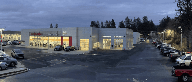 Exterior view of the Wendle Nissan dealership and service center in Spokane, WA, featuring a large inventory of new and used cars and SUVs under evening lights.