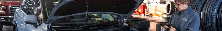 A service advisor at the Wendle Nissan service center using a digital diagnostic tablet while inspecting a vehicle with its hood open.