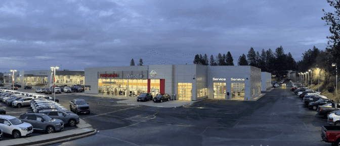 Wide view of the Wendle Nissan dealership in Spokane at dusk, showing the lit showroom, service bays and parking lot.