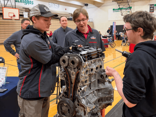 A group of students and instructors posing for a photo together at a trades night event inside a bright workshop.