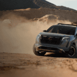 A grey Nissan Pathfinder Rock Creek kicking up dust while driving off-road over a rugged, rocky desert terrain.