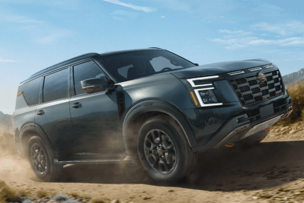 Dark gray Nissan Armada SUV kicking up dust as it navigates a dirt off-road path against a clear blue sky.