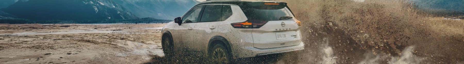 White AWD 2026 Nissan Rogue driving through muddy terrain, demonstrating all-weather capabilities.