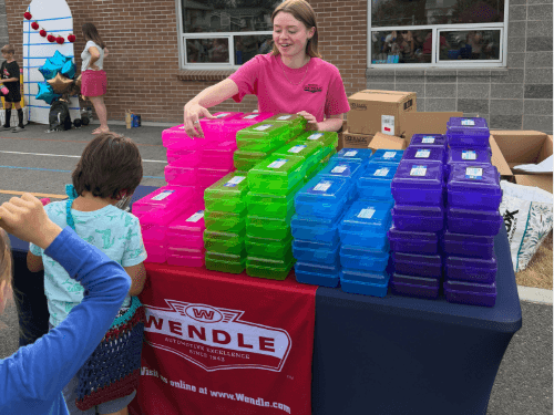Wendle team member handing out colorful school supply boxes at a community event near Shiloh Hills.