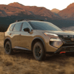 Nissan Rogue Rock Creek driving on an off-road trail through a field with rugged mountain peaks in the background.