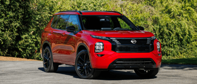 Red 2026 Nissan Rogue Plug-In Hybrid SUV parked outdoors with green foliage in the background.